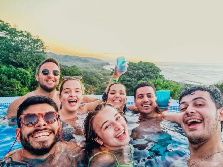 A group of people sharing drinks in a pool overlooking a green landscape.
