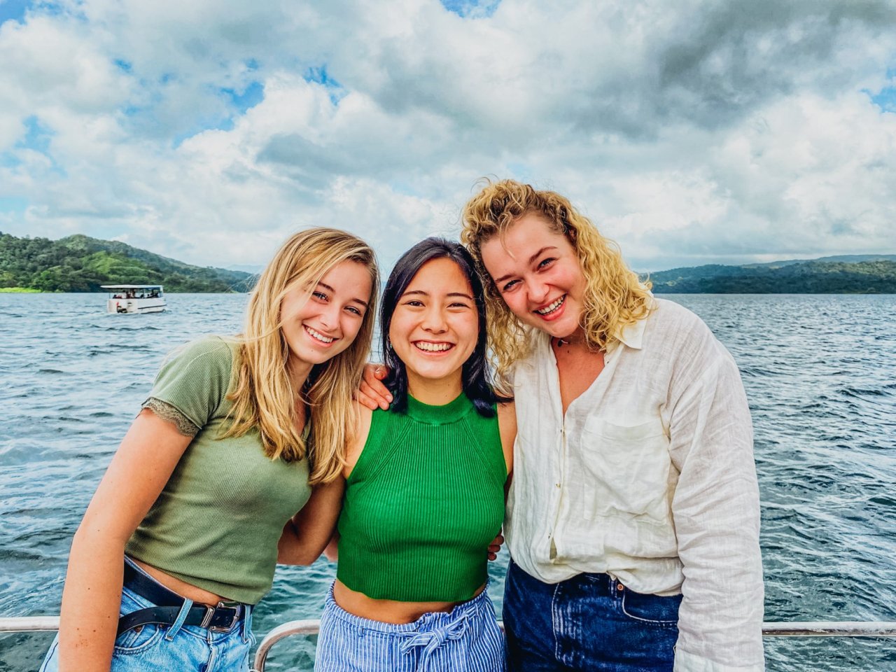 Three young people enjoying a boat ride with a distance view of Costa Rica's green landscape.