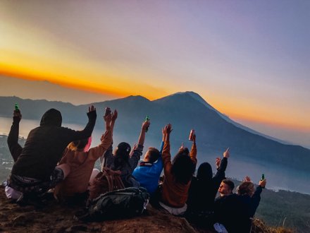 A group marvelling at the view after hiking Mount Batur for sunrise with mountains in view and the golden orange sunrise in the background