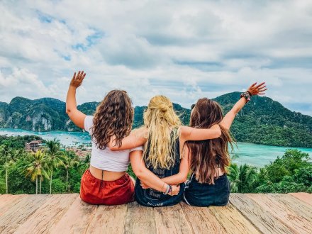 Three girls admiring the view at the top of the viewpoint in Koh Phi Phi, Thailand admiring the view of the crystal clear blue ocean and luscious greenery