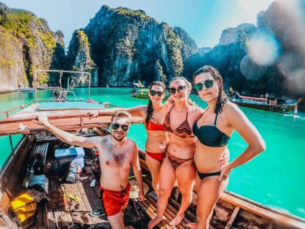 A group of four on a long tail boat in Koh Phi Phi, Thailand surrounded by lush greenery, cliffs and stunning turquoise water
