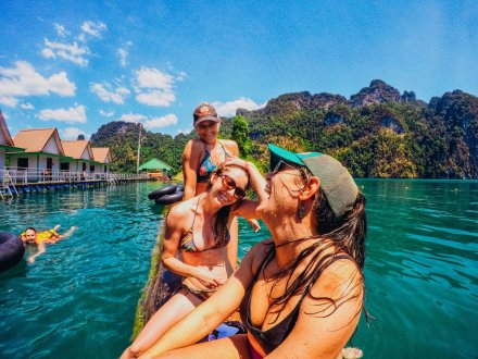 Three girls sitting on the log in the lake at Khao Sok National park Thailand 
